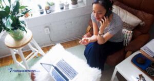 birds eye view perspective of a woman sitting in a chair using a laptop while on the phone and using credit card